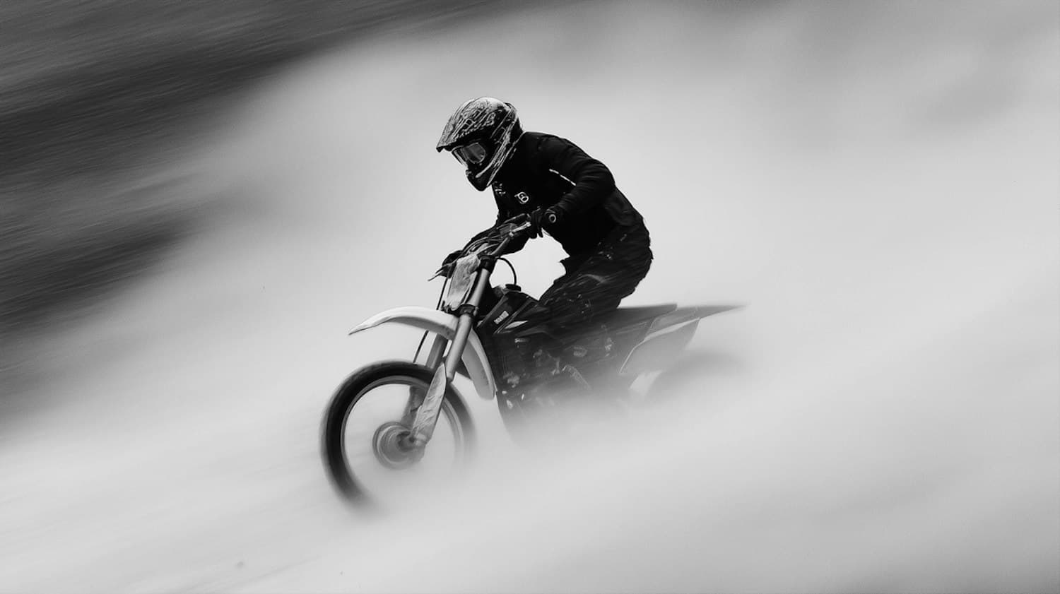 A motorcyclist riding through a cloud of dust, in black and white